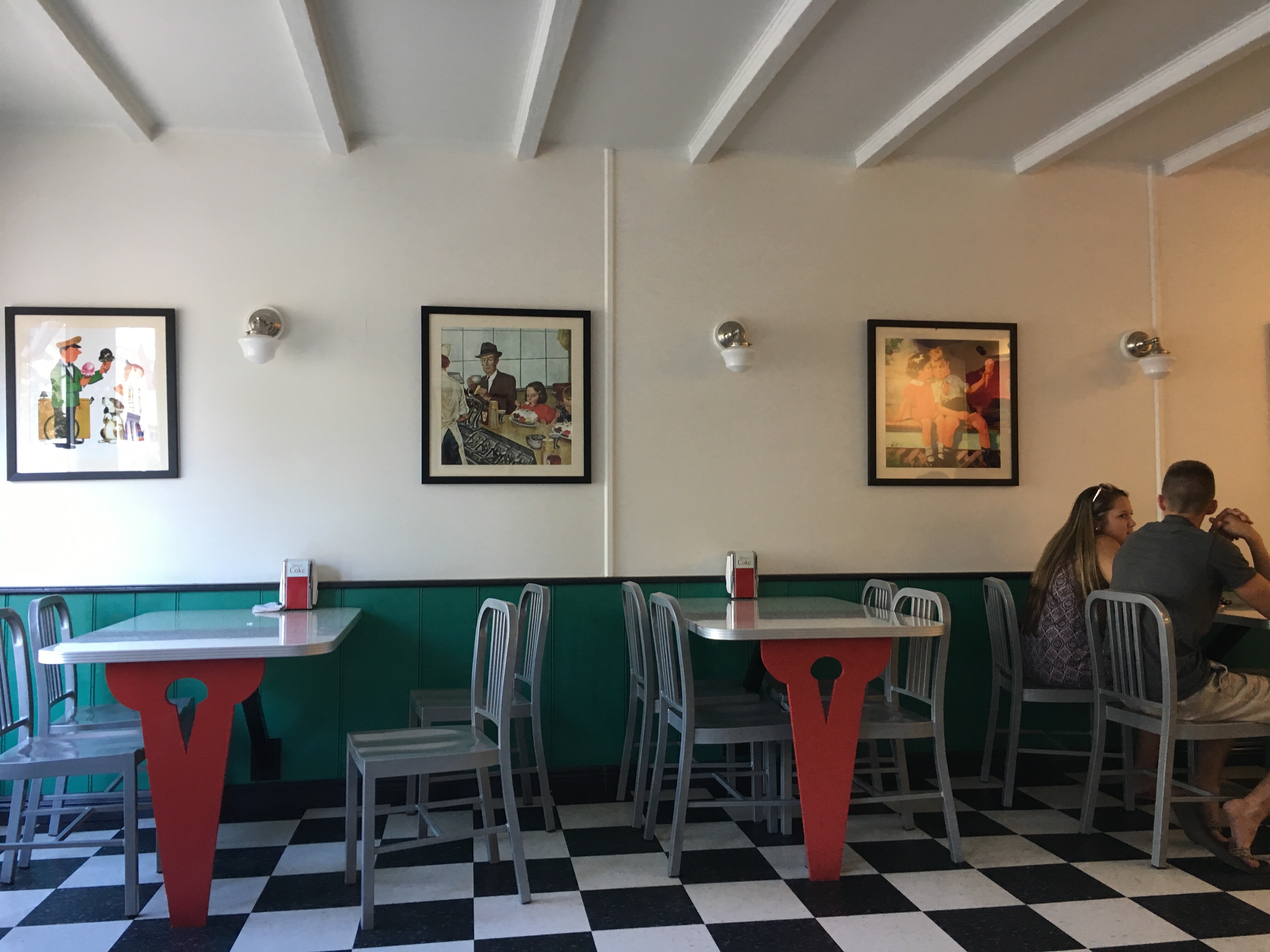 Two 50s style tables and Norman Rockwell paintings near an ice crema bar